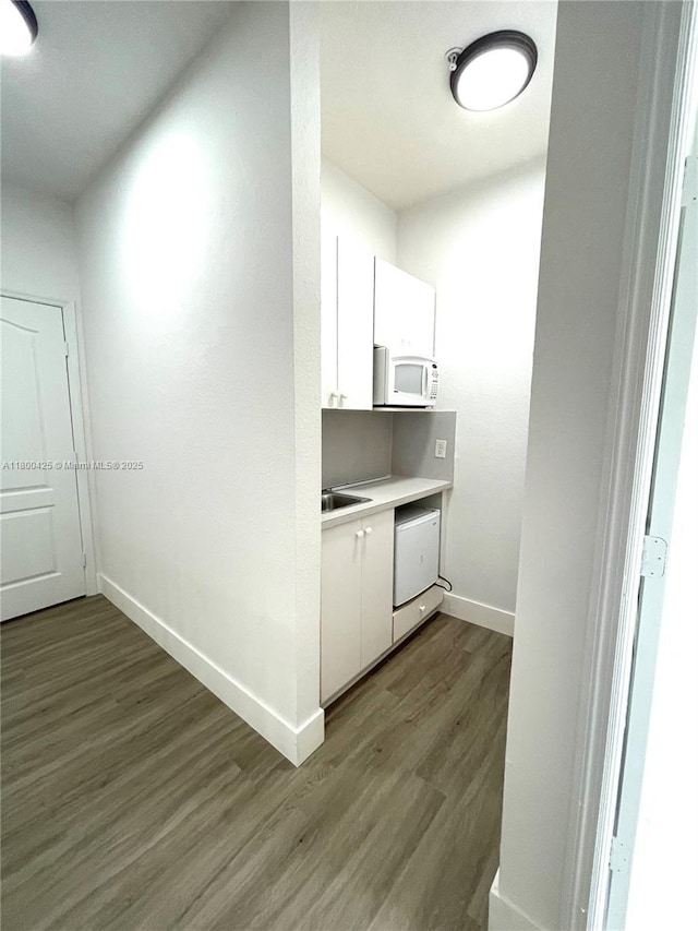 kitchen with white appliances, dark wood finished floors, white cabinetry, and baseboards