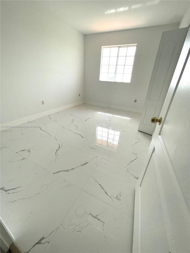 unfurnished room featuring marble look tiles and baseboards