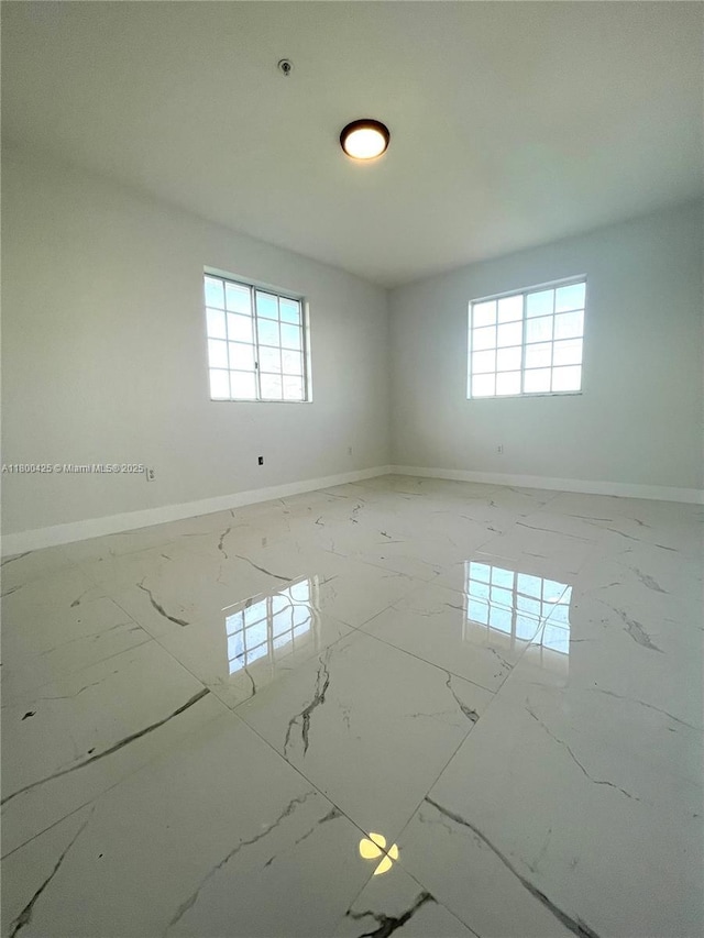 empty room featuring healthy amount of natural light, marble finish floors, baseboards, and fire sprinkler in ceiling