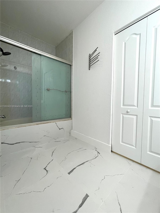 bathroom with marble look tiles, a shower with door, and baseboards