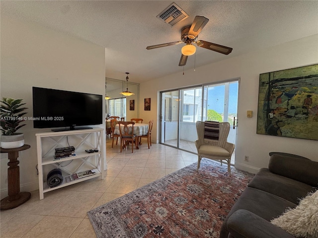 living area featuring light tile patterned floors, ceiling fan, a textured ceiling, and baseboards