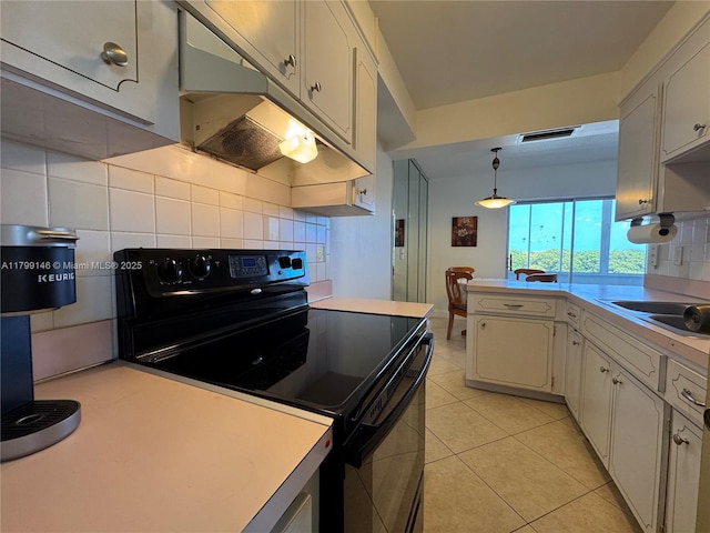 kitchen with black electric range oven, tasteful backsplash, a peninsula, light countertops, and light tile patterned floors