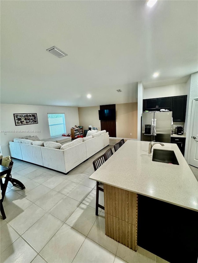 kitchen with dark cabinets, stainless steel fridge with ice dispenser, a sink, light tile patterned floors, and recessed lighting