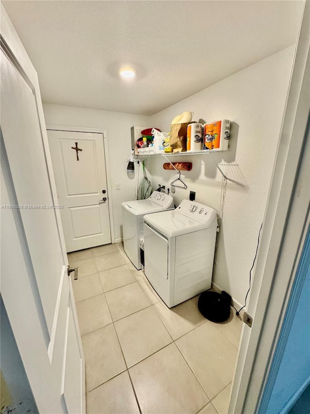laundry room featuring washing machine and clothes dryer, light tile patterned floors, and a textured ceiling