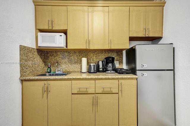 kitchen with freestanding refrigerator, a sink, white microwave, backsplash, and light countertops