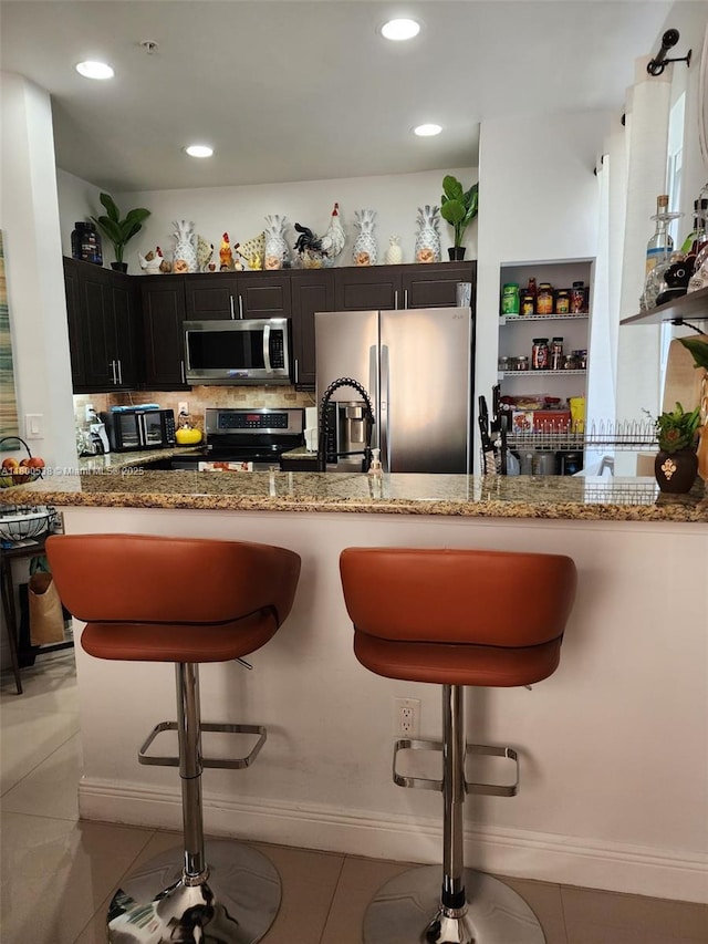 12430 SW 50th St Unit 147, Miramar, FL 33027 - kitchen featuring appliances with stainless steel finishes, light stone countertops, a breakfast bar area, light tile patterned flooring, and recessed lighting