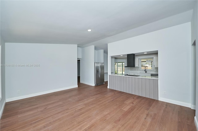 unfurnished living room with light wood-style flooring, a sink, baseboards, and recessed lighting