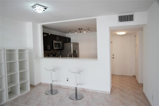 kitchen with appliances with stainless steel finishes, light countertops, tasteful backsplash, dark cabinets, and baseboards
