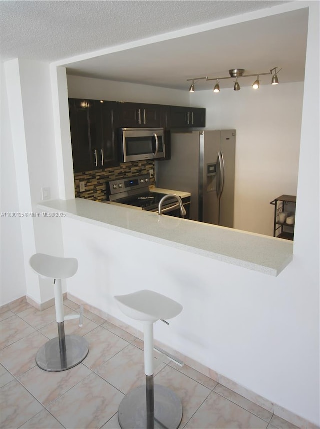 kitchen featuring stainless steel appliances, dark cabinets, backsplash, rail lighting, and light countertops