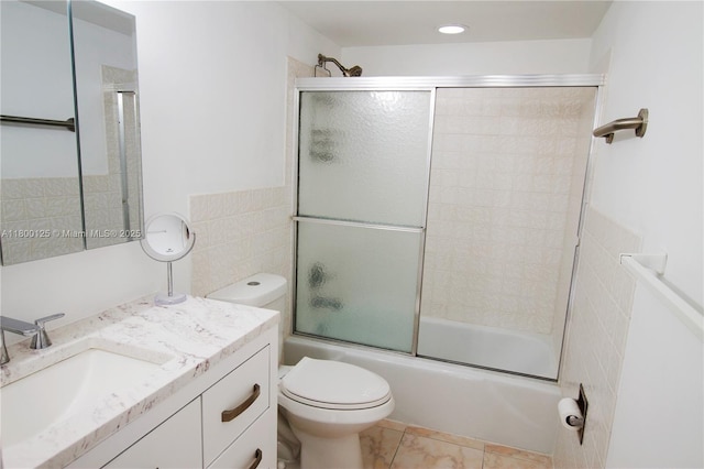 bathroom featuring bath / shower combo with glass door, toilet, vanity, tile patterned flooring, and tile walls