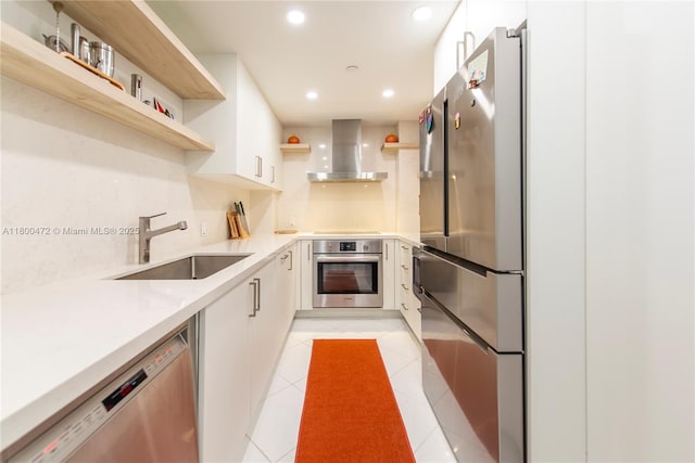 kitchen featuring open shelves, wall chimney exhaust hood, appliances with stainless steel finishes, a sink, and light countertops