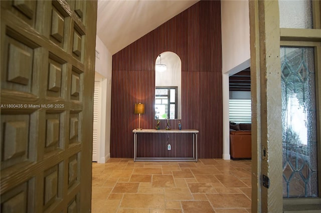 hallway with stone tile flooring, high vaulted ceiling, and arched walkways