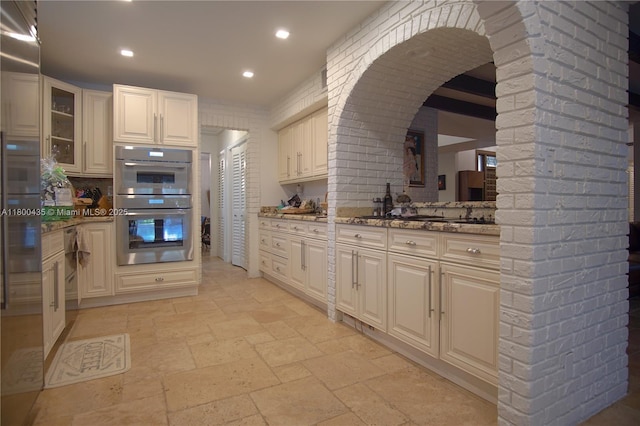 kitchen featuring stone tile flooring, glass insert cabinets, appliances with stainless steel finishes, stone countertops, and arched walkways