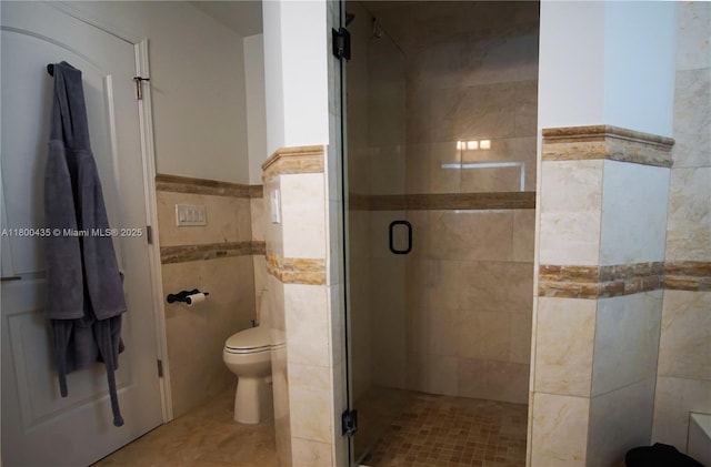 bathroom featuring a stall shower, tile walls, toilet, and a wainscoted wall