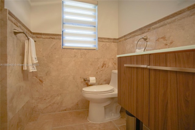 bathroom with toilet, tile patterned flooring, tile walls, and a wainscoted wall