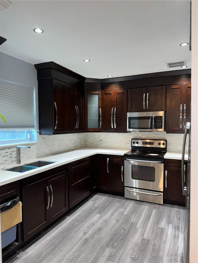 kitchen featuring stainless steel appliances, a sink, light wood finished floors, light countertops, and decorative backsplash