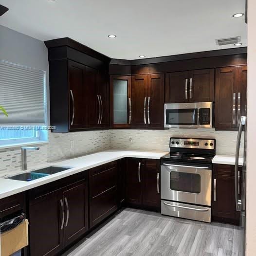 kitchen with appliances with stainless steel finishes, a sink, light countertops, backsplash, and recessed lighting