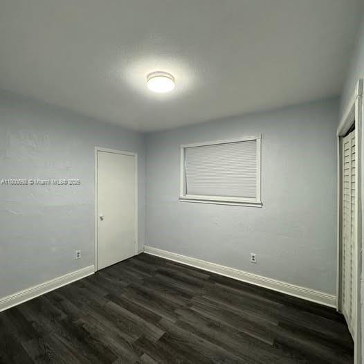 unfurnished bedroom with baseboards and dark wood-style floors