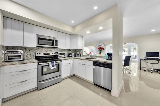1060 SW 111th Way, Davie, FL 33324 - kitchen with stainless steel appliances, arched walkways, white cabinets, decorative backsplash, and light stone countertops