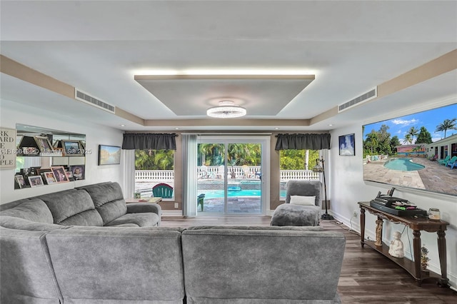 living area with a raised ceiling, dark wood finished floors, and baseboards
