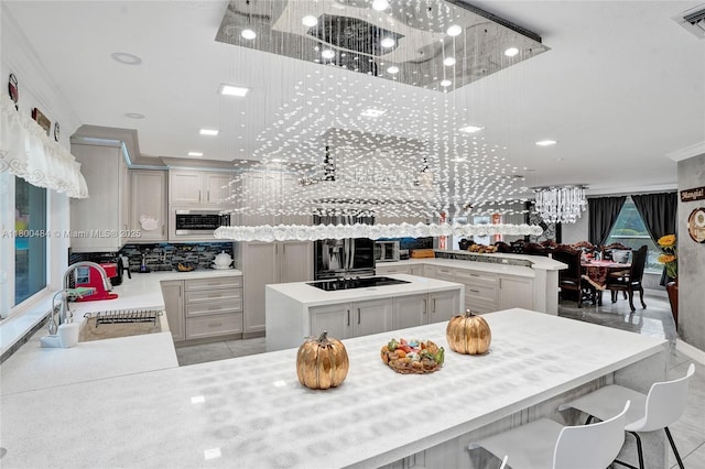 kitchen featuring a sink, black electric cooktop, decorative backsplash, a center island, and a chandelier