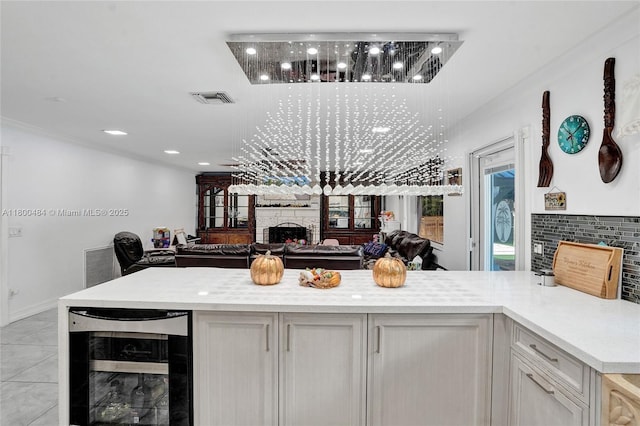 kitchen featuring a stone fireplace, beverage cooler, light countertops, ornamental molding, and open floor plan