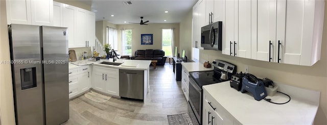 kitchen featuring appliances with stainless steel finishes, open floor plan, ceiling fan, white cabinetry, and light countertops