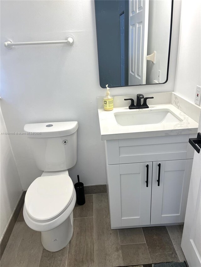 half bath featuring baseboards, vanity, and toilet