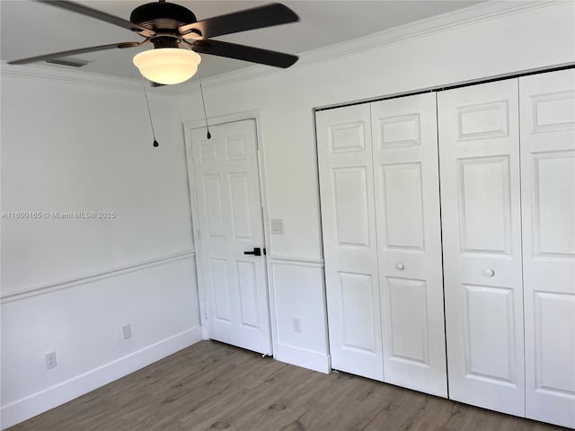 unfurnished bedroom with ornamental molding, wood finished floors, baseboards, ceiling fan, and a closet