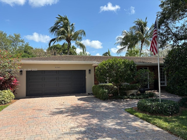 ranch-style home with decorative driveway, an attached garage, and stucco siding
