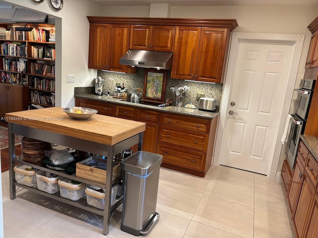 kitchen with under cabinet range hood, light tile patterned floors, backsplash, and black electric stovetop
