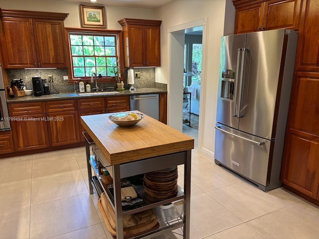kitchen featuring appliances with stainless steel finishes, a sink, tasteful backsplash, light tile patterned floors, and butcher block counters