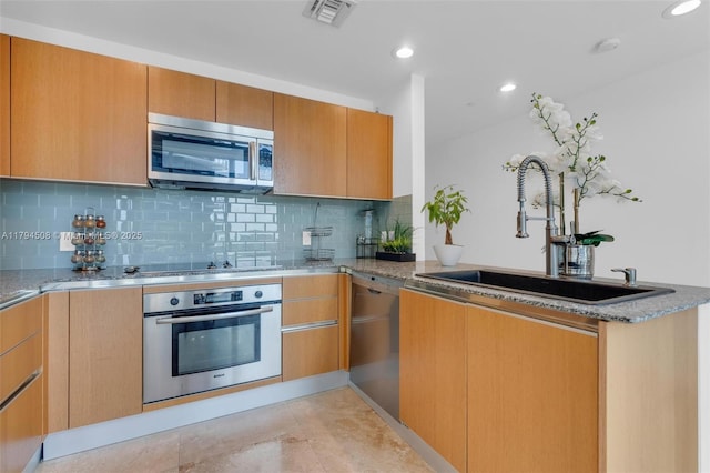 kitchen with stainless steel appliances, a sink, light stone counters, a peninsula, and backsplash