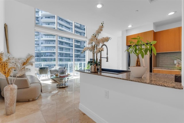 kitchen with backsplash, dark stone counters, recessed lighting, brown cabinets, and light marble finish flooring