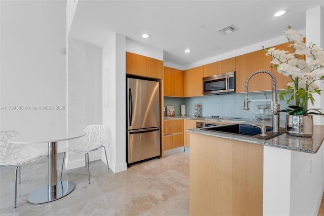kitchen featuring stainless steel appliances, light stone countertops, a sink, a peninsula, and recessed lighting