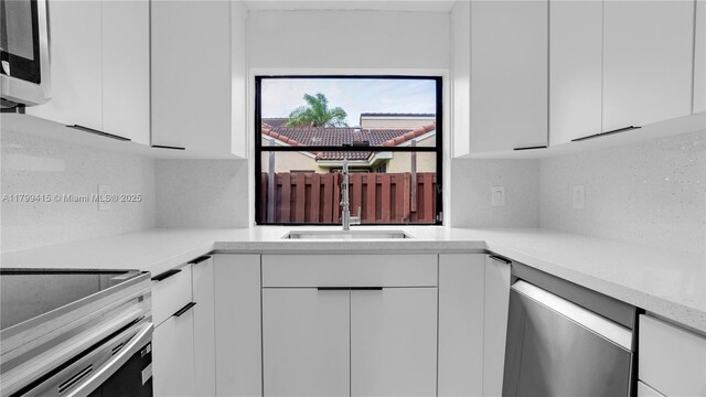 kitchen featuring appliances with stainless steel finishes, white cabinetry, and a sink