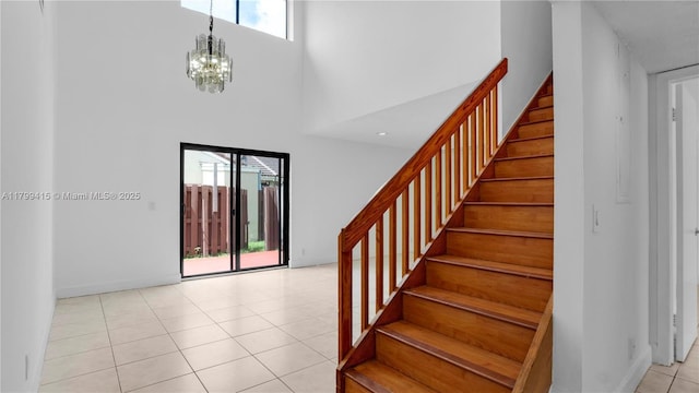 entryway featuring a towering ceiling, stairs, a chandelier, light tile patterned flooring, and baseboards