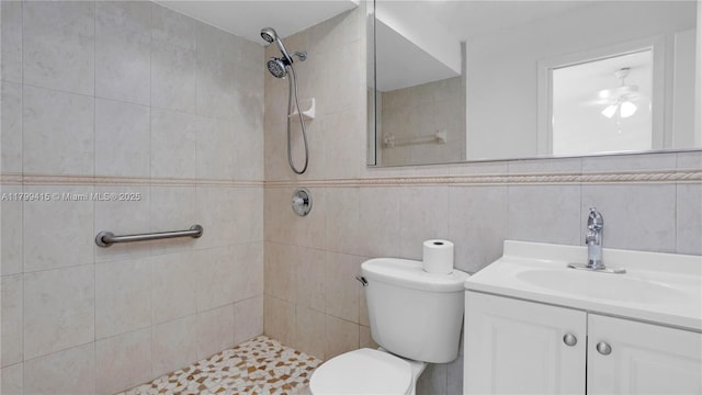 full bathroom featuring tiled shower, toilet, vanity, a ceiling fan, and tile walls