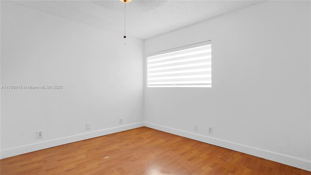 spare room with baseboards, light wood-type flooring, and a textured ceiling
