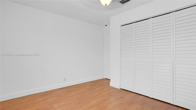 unfurnished bedroom featuring light wood-style floors, baseboards, and a closet