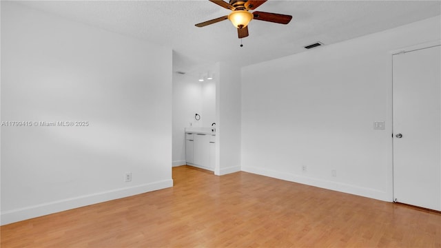 spare room with ceiling fan, light wood finished floors, baseboards, and a textured ceiling
