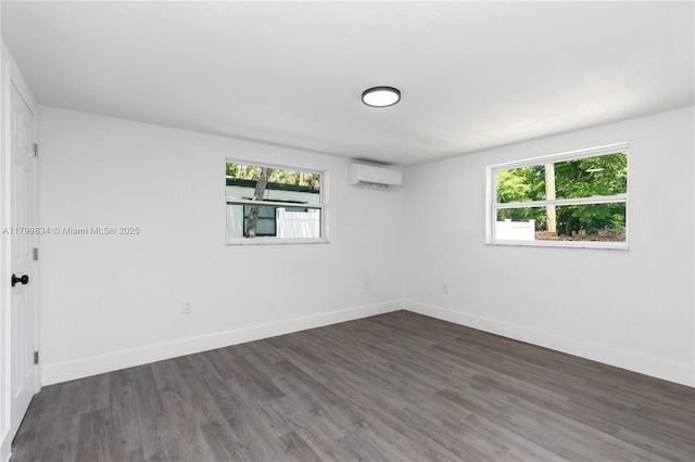 spare room featuring an AC wall unit, plenty of natural light, wood finished floors, and baseboards