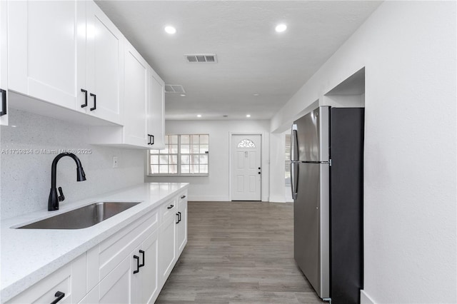kitchen with freestanding refrigerator, a sink, white cabinets, light wood-type flooring, and recessed lighting