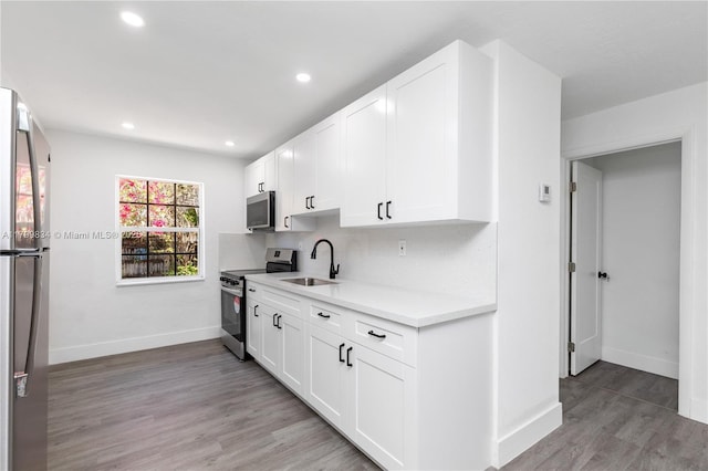 kitchen with appliances with stainless steel finishes, a sink, light countertops, baseboards, and white cabinetry