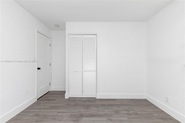 unfurnished bedroom featuring baseboards, wood finished floors, and a closet