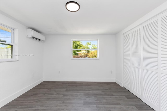 unfurnished bedroom featuring a wall mounted air conditioner, baseboards, a closet, and wood finished floors