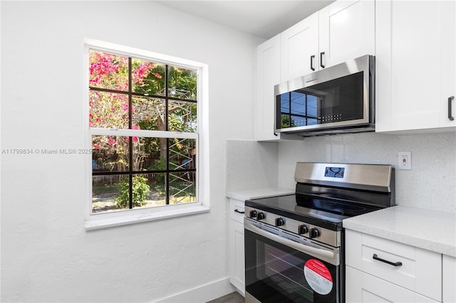 kitchen with stainless steel appliances, plenty of natural light, white cabinetry, and baseboards
