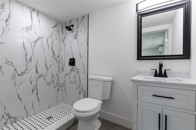 bathroom with toilet, a marble finish shower, wood finished floors, vanity, and baseboards