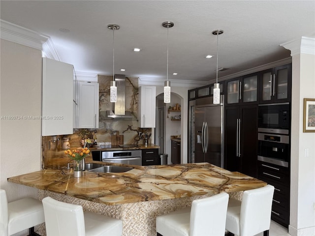 8389 NW 115th Ct, Doral, FL 33178 - kitchen with wall chimney exhaust hood, built in appliances, a peninsula, arched walkways, and a breakfast bar