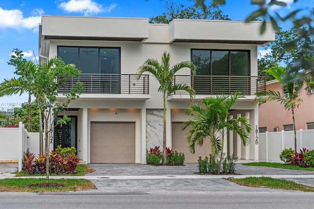 contemporary home with a balcony, an attached garage, stucco siding, fence, and driveway